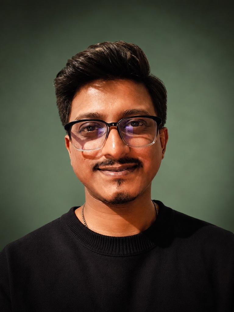 Tanmoy Pal, wearing glasses and a black sweater against a green background